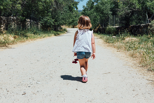 Blond hair girl in shorts walking on a dirt road in summer