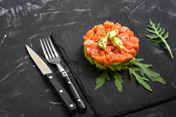 ensalada de salmón fresco, aguacate y rúcula en un anillo culinario sobre un plato de pizarra, fondo de hormigón negro. tartar de salmón crudo. enfoque selectivo. - seviche prepared ahi freshness mexican culture fotografías e imágenes de stock