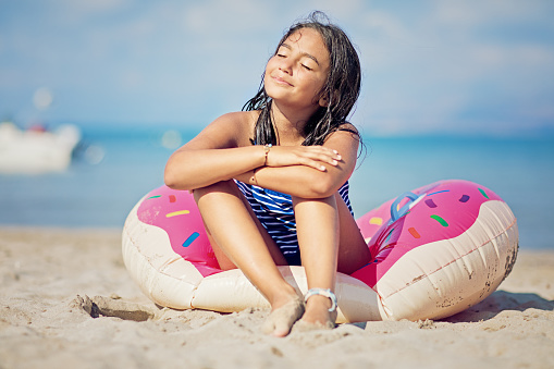 Happy girl is sitting on beach and enjoying the sun