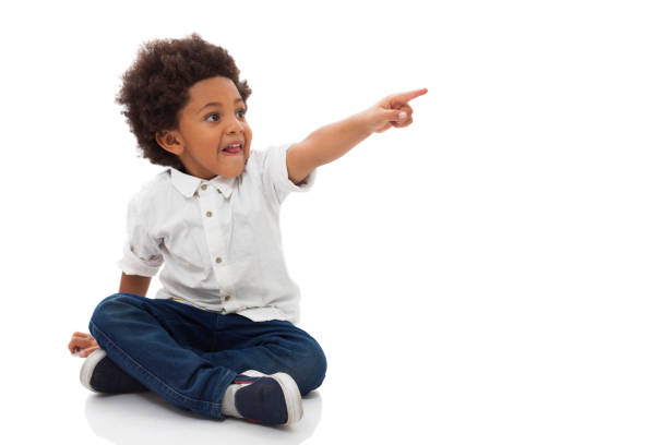 istock Surprised black little boy pointing away sitting on floor smiling 1252756527
