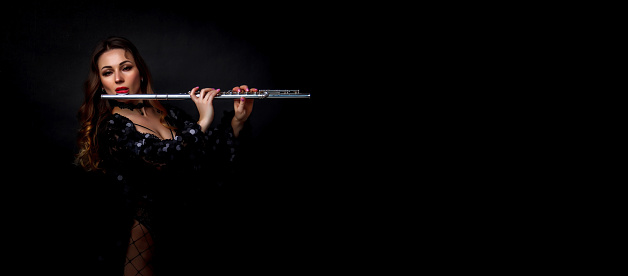 Female girl artist in suit with flute on black background. Flute in hand. Player with orchestra music instrument. Isolated on black. Author's space. Large background space for an inscription or logo