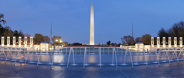 Nighttime panoramic view of the Washington monument and the World War II Memorial located on the National Mall in Washington DC. The Washington monument (c. 1884) is the tallest obelisk in the world. The World War II memorial (c. 2004) features pillars, triumphal arches and fountains honoring veterans of WWII.