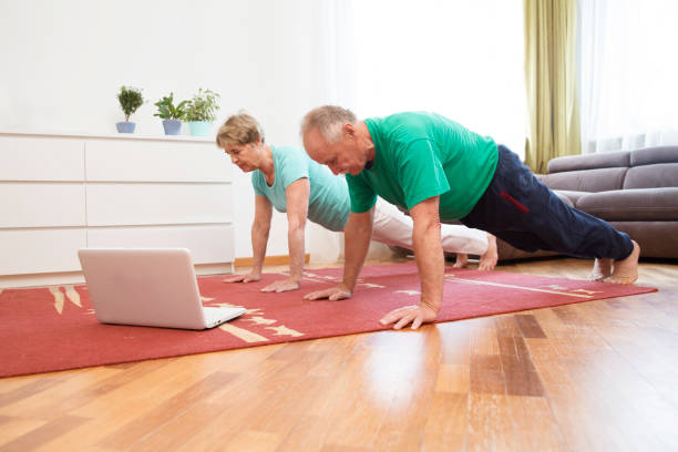 aktywna para seniorów robi trening fitness w salonie w domu z laptopem.  treningi zdalne.  siłownia domowa. fitness, activewear. - senior adult healthy lifestyle athleticism lifestyles zdjęcia i obrazy z banku zdjęć