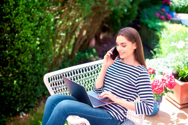 istock Attractive young woman using mobile phone and laptop while sitting balcony at home 1252775258