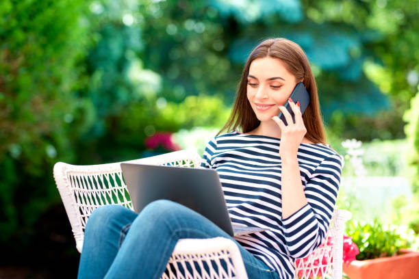 istock Attractive young woman using mobile phone and laptop while sitting balcony at home 1252775276