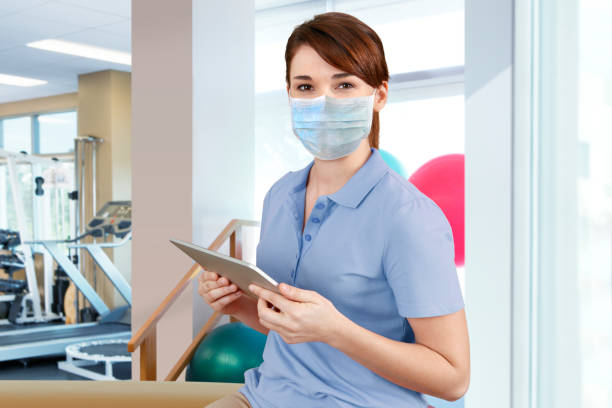 istock Female Physical Therapist Wearing Protective Mask Charting on Digital Tablet 1252775409