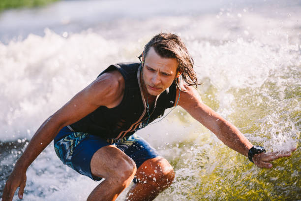 Active wakesurfer jumping on wake board down the river waves. Surfer on wave. Male athlete training on wakesurf training. Active water sports in open air on board. A man catches a wave on surf. wakesurfer activo saltando en el tablero de estela por las olas del río. surfista en la ola. entrenamiento de atleta masculino en el entrenamiento de vigilia. deportes acuáticos activos al aire libre a bordo. un hombre atrapa una ola en surf.