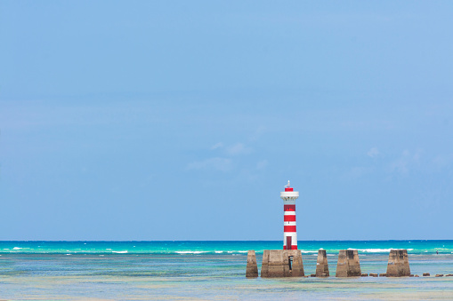A beautiful idyllic turquoise landscape with a red and White striped Lighthouse over Atlantic ocean in Maceio, Brazil in a sunny summer day.