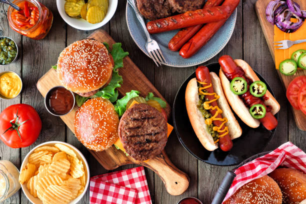 핫도그와 햄버거 뷔페가 있는 여름 바비큐 푸드 테이블 장면, 어두운 나무 위에서 최고 전망 - burger barbecue grill hamburger grilled 뉴스 사진 이미지