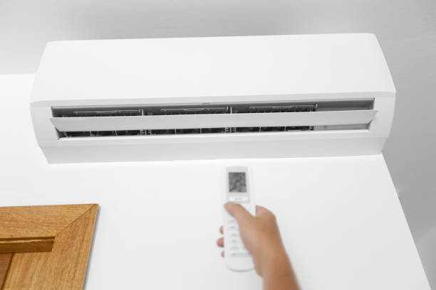 istock Flat air conditioner on white wall in room interior. Man pushing button on remote 1252796927