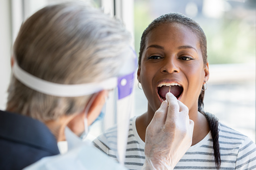 La mujer abre la boca para el hisopo de la mejilla y la garganta mientras se le hace la prueba del coronavirus De Covid-19 photo