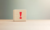Exclamation Point Written Wood Block Sitting on Wood Surface in Front a Defocused Background