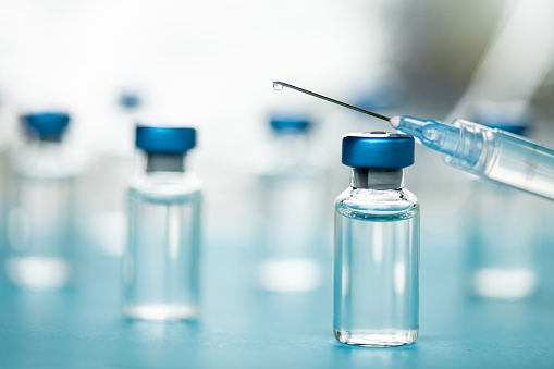 Vaccine, injectable medicine or drug vials and syringe close up in blue tones