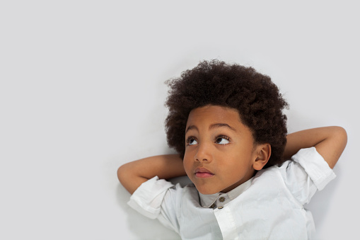 Black little boy lying down daydreaming while looking away