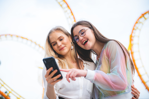 Friends group relaxing and taking selfie with smartphone at an amusement theme park, concept of happy and hangout carnival