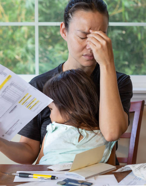 Stressed mother with her child in her lap stressing out about paying utility bills Woman is being stressed out over paying bills and her daughter is comforting her family mother poverty sadness stock pictures, royalty-free photos & images