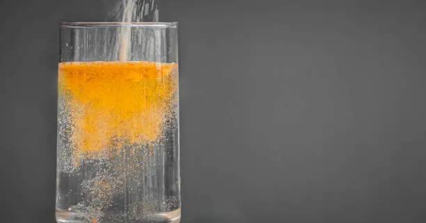 Action shot of an orange powdered drink mix being poured into a clear glass of water