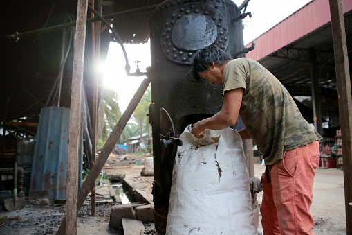 A Nepalese ethnicity man is taking out planks from a big bag. The planks are meant for burning inside an antique burner to produce energy and steam for eight hours mushroom growth packs sterilization in Malaysia.