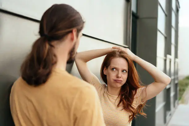 Young woman looking at her boyfriend in disbelief puffing out her cheeks with a sideways glance as they chat on an urban street