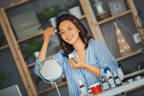 Skin care routine. Young woman applying serum on her face while looking at mirror.. face serum stock pictures, royalty-free photos & images