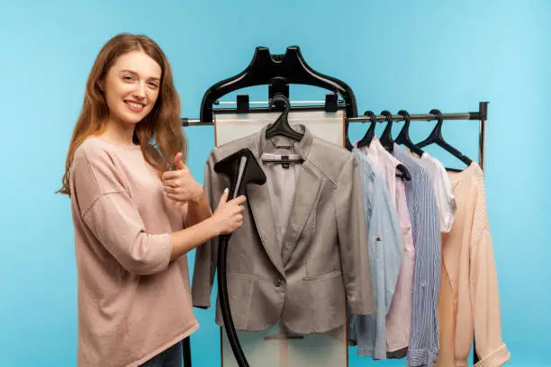Satisfied housewife steaming business suit at dry-cleaner and showing thumbs up, recommending professional services washing, cleaning and ironing clothes, care of fabric. indoor studio shot isolated