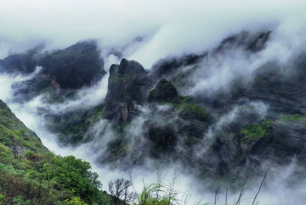 Mountain cliff with greenery and clouds during monsoon season at Tamhini Ghat viewpoint Maharashtra. Western ghats at the start of monsoon season.