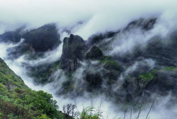 Mountain cliff with greenery and clouds during monsoon season at Tamhini Ghat viewpoint Maharashtra. Western ghats at the start of monsoon season. Mountain cliff with greenery and clouds during monsoon season at Tamhini Ghat viewpoint Maharashtra. Western ghats at the start of monsoon season. maharashtra stock pictures, royalty-free photos & images
