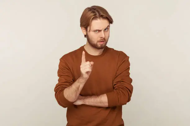 Photo of Be careful! Portrait of strict teacher, bossy man with beard wearing sweatshirt standing with admonishing gesture