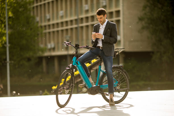 giovane uomo d'affari sull'ebike con cellulare - bicicletta elettrica foto e immagini stock