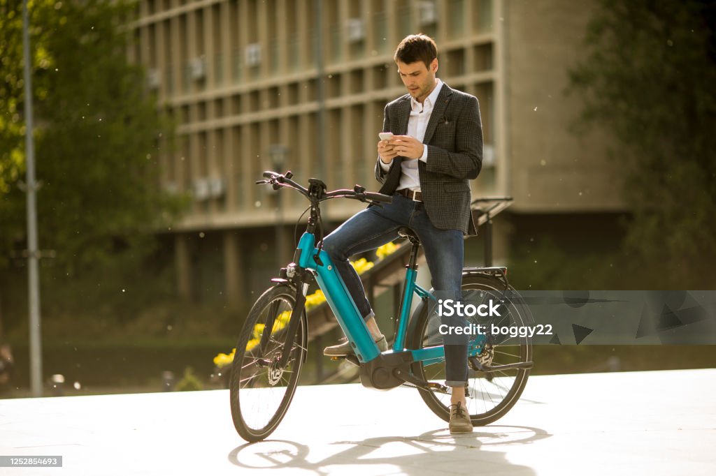 Young businessman on the ebike using mobile phone Handosme young businessman on the ebike using mobile phone Electric Bicycle Stock Photo