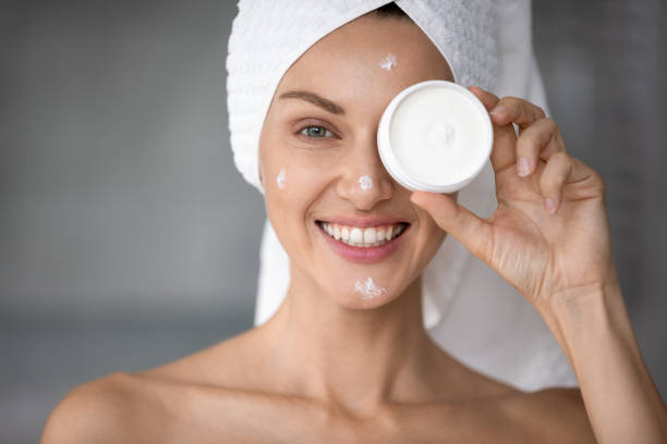 istock Smiling young woman using moisturizing face cream in bathroom 1252855096