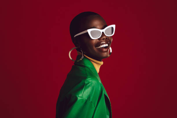Beautiful woman wearing stylish sunglasses Beautiful woman wearing stylish sunglasses and smiling against red background. African female model wearing funky sunglasses. funky stock pictures, royalty-free photos & images