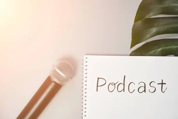 Podcast concept. White notebook with blank sheet. Black microphone and green monstera leaf. Audiobook and podcasting. Audio technology. Home school teaching.