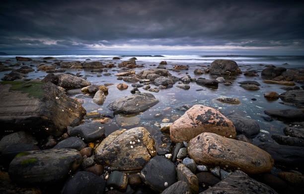 Rocks on the coastline, in the background you see the sea emerge and the sky is filled with clouds.