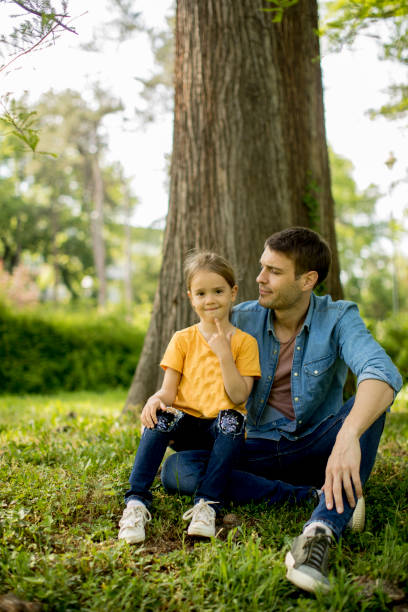 istock Single father sitting on grass by the tree with little daughter 1252867856