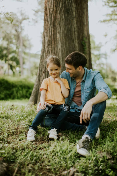 istock Single father sitting on grass by the tree with little daughter 1252867858