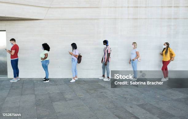Multiracial People Standing In A Queue And Waiting Young People With Social Distancing And Wearing Protective Face Masks Concept Of The New Normality And Social Distancing Stock Photo - Download Image Now