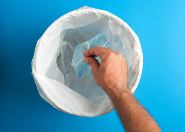 istock covid-19 prevention concept, used mask putting it with the hands inside trash, blue background 1252876506