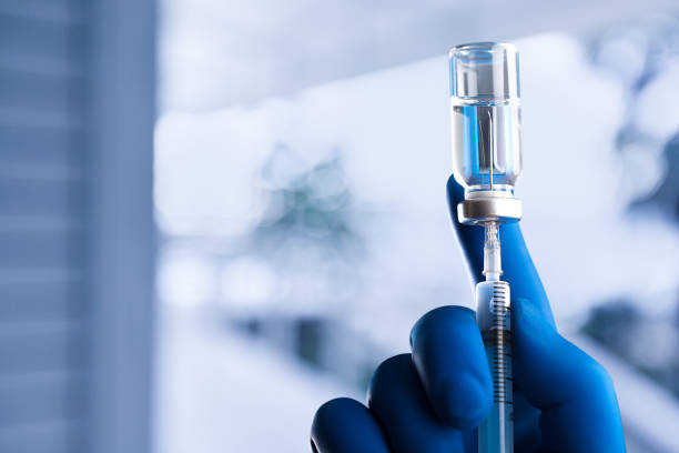 A medical hand in a glove holds an ampoule with a vaccine and a syringe with illustration The hands in blue glove of the scientist hold the processor hormone photos stock pictures, royalty-free photos & images