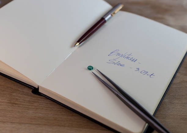istock Emerald gemstone on a notebook with notes, jewelry clips and pen 1252884540