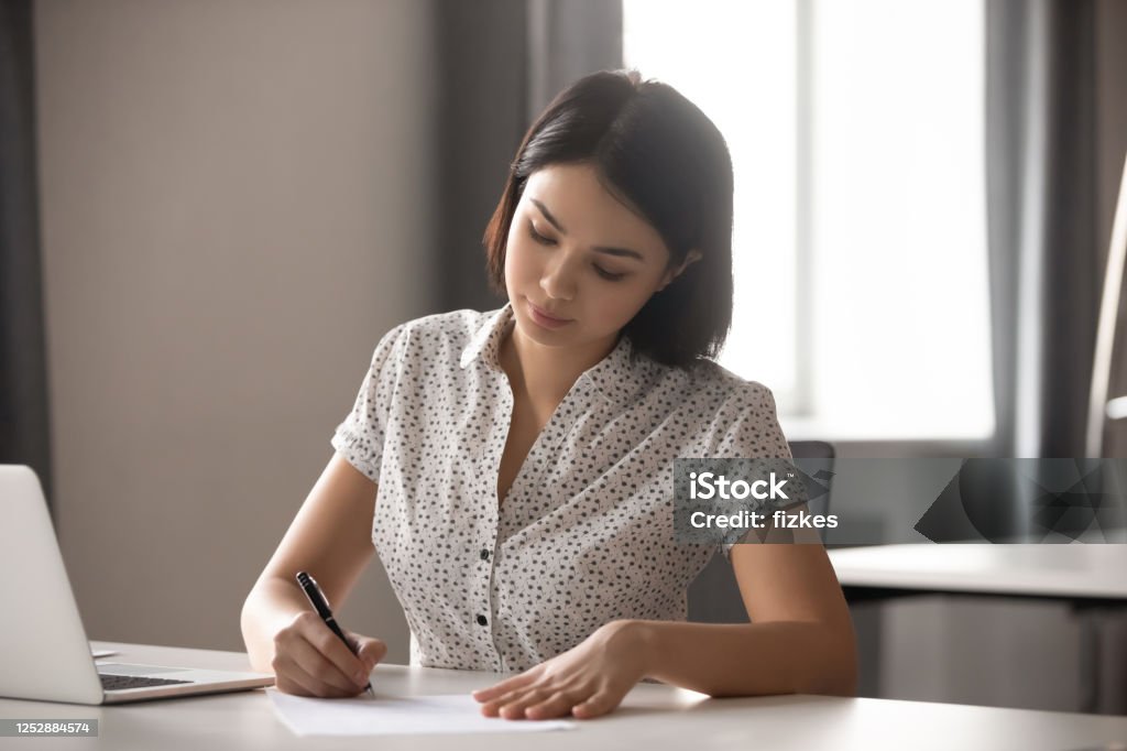 Concentrated young asian business woman signing important contract. Concentrated young asian business woman leader working with financial reports, signing important documents, contract or agreement. Focused company executive manager making deal with corporate client. Assertiveness Stock Photo