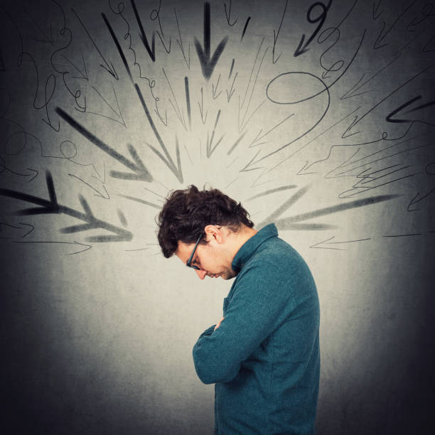 persona introversa sconvolta che guarda in basso turbata, si sente costernata. ragazzo solitario che sta vivendo una crisi emotiva. l'uomo è sotto pressione sul posto di lavoro come frecce multiple sul muro che lo indicano. - embarrassment men business guilt foto e immagini stock