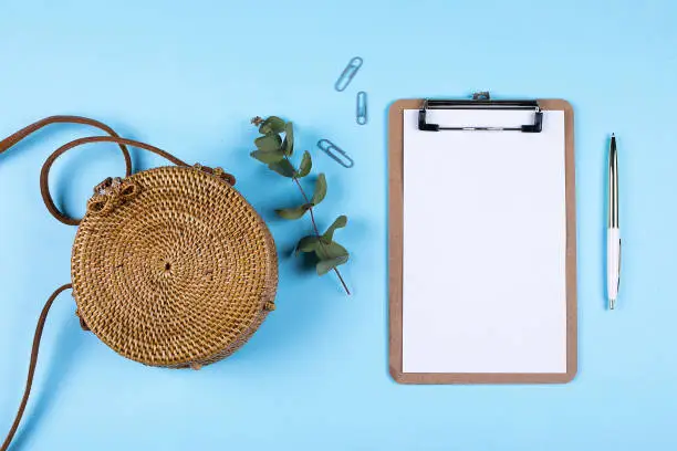 Photo of Flat lay composition with rattan bag, eucalyptus and empty clipboard. Top view, copy spase. Mockup concept.