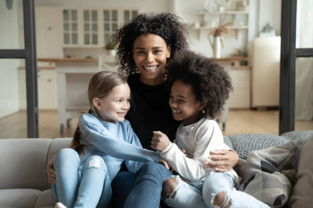 istock Cheerful African mother sitting on couch embraces multiracial daughters 1252896405