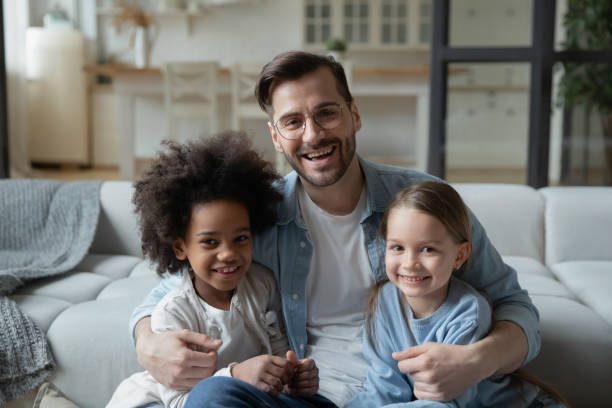 istock Father sit on sofa hugs caucasian and african little daughters 1252896416