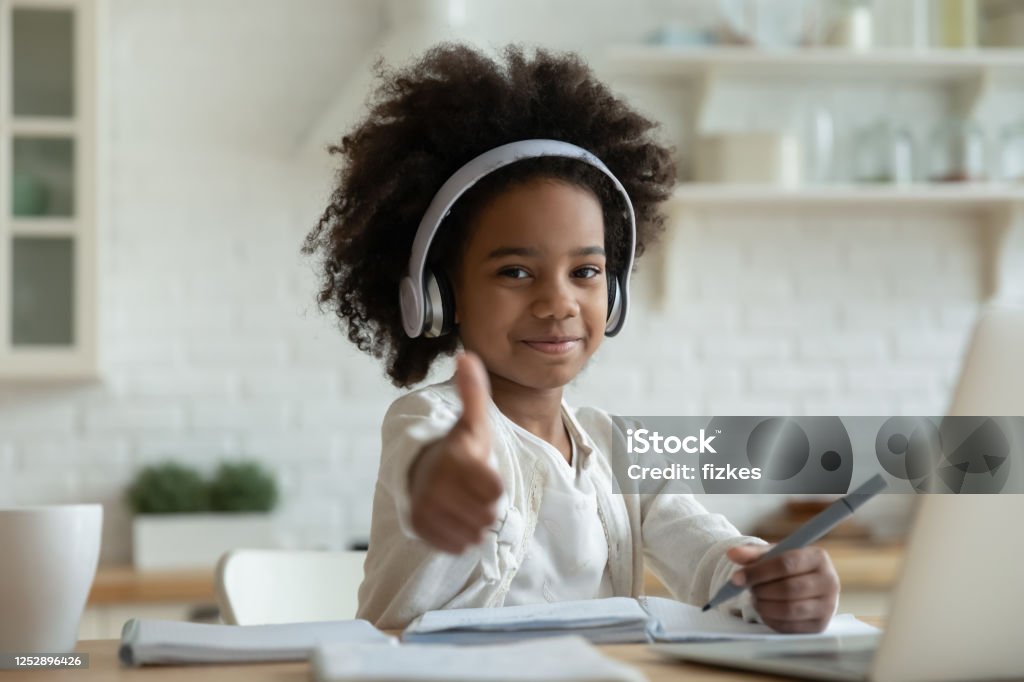 African girl in headphones enjoy showing thumbs up e-learning African girl in headphones enjoy e-learn sit at table showing thumbs up recommend e-study easy and interesting app for children, using modern tech. Homeschooling, clever kid and self-education concept Child Stock Photo