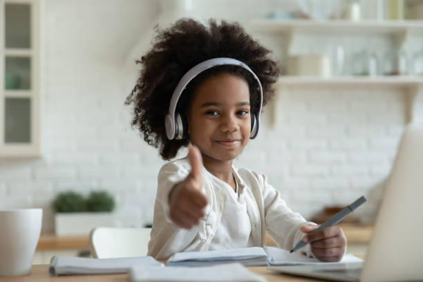 African girl in headphones enjoy showing thumbs up e-learning African girl in headphones enjoy e-learn sit at table showing thumbs up recommend e-study easy and interesting app for children, using modern tech. Homeschooling, clever kid and self-education concept homework photos stock pictures, royalty-free photos & images