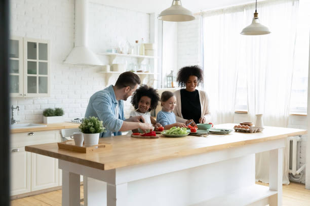 ครอบครัวข้ามชาติมีความสุขกับเด็กเตรียมสลัดผักในห้องครัว - family dinners and cooking ภาพสต็อก ภาพถ่ายและรูปภาพปลอดค่าลิขสิทธิ์