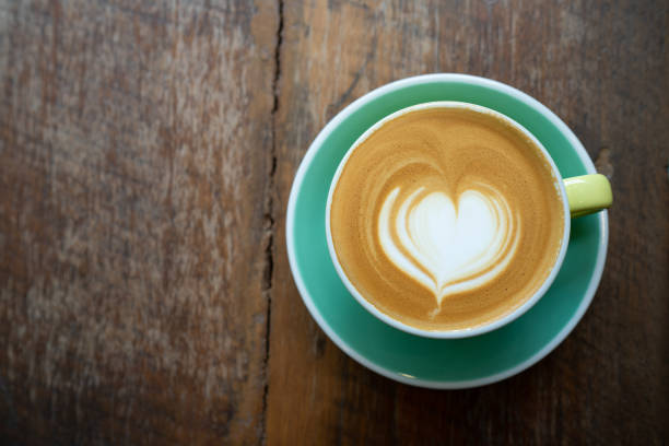Top view of Latte coffee or cappuccino coffee in green cup with heart latte art on wooden table.