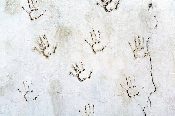 istock Old dirty white cement wall with handprints in dark paint with drips and cracks. Pattern of random palm prints on the texture of concrete. 1252898229